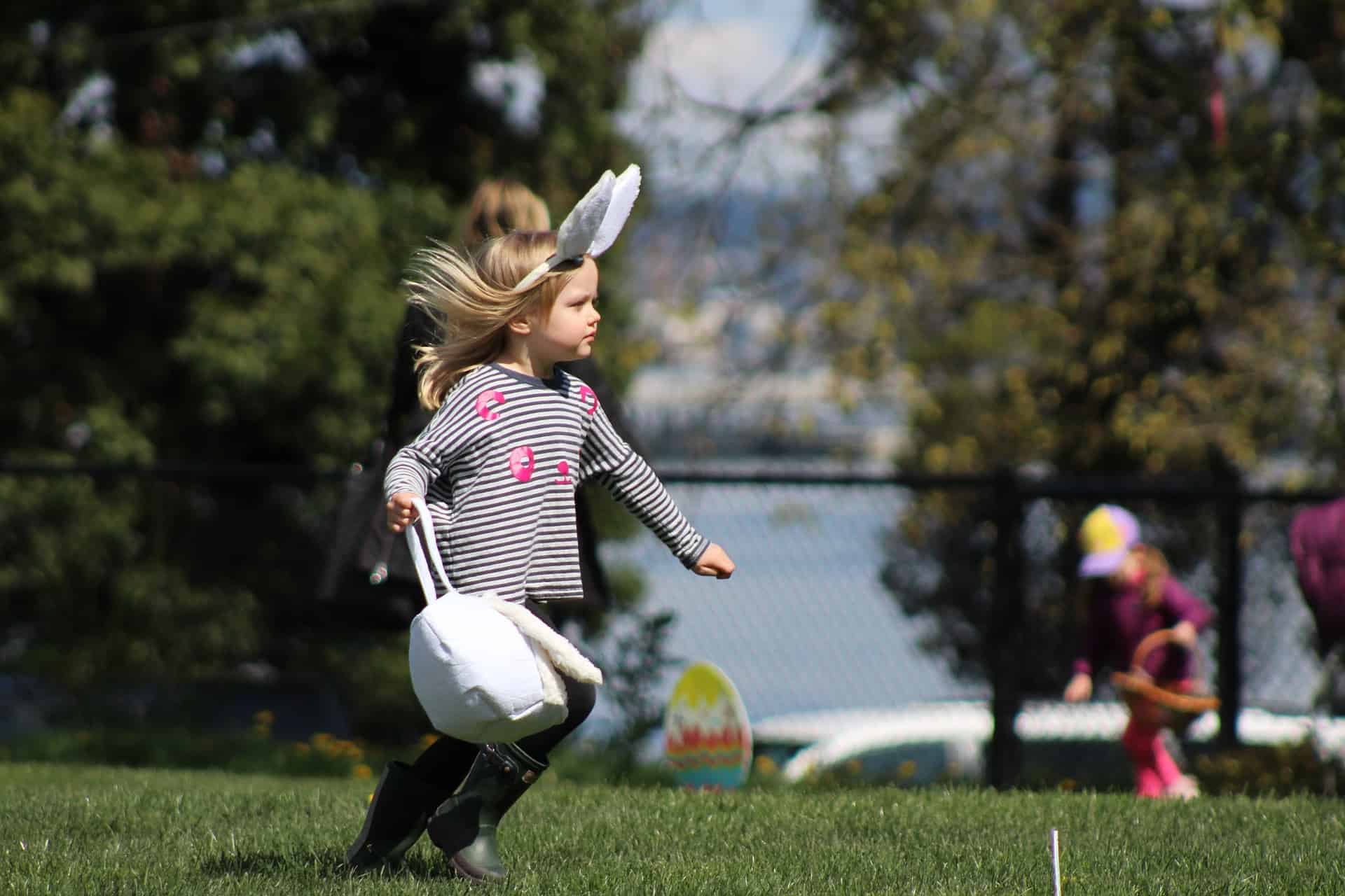 Little girl in bunny ears hunting for Easter eggs